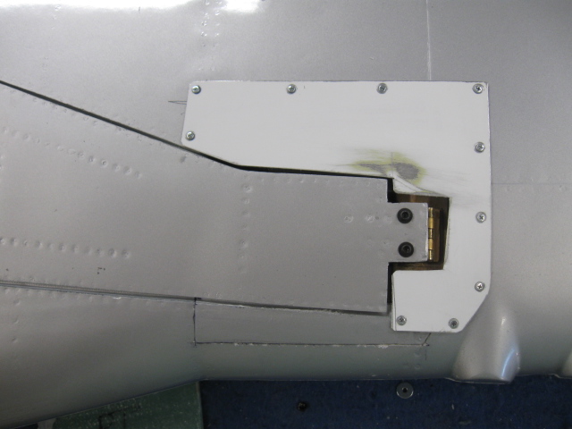 To replace the cut-out composite parts and still permit access, thin lithoplate sheet is used and held in place with small sheet metal screws. Then painted. A small portion of the cut-out composite wing was reglued at the leading edge. 